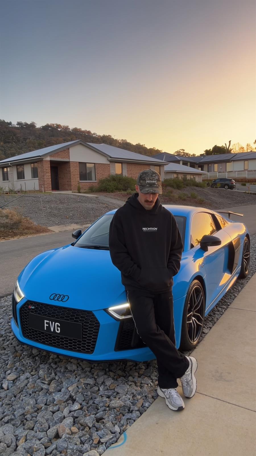 James leaning on his blue Audi R8 at sunset