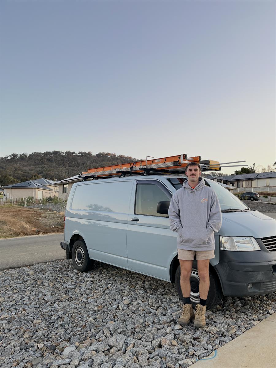 James in his work gear standing in front of his tradie van with ladders on the roof